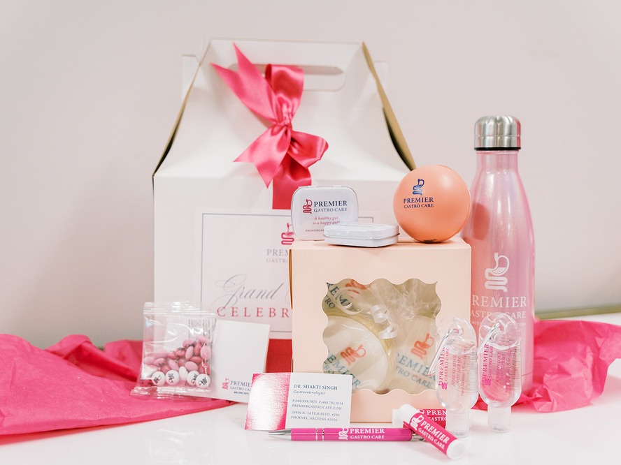 Pink and white Premier Gastro Care grand-opening gift box with branded water bottle, mints, lip balm, pen and hand sanitizer, designed by Be In Love Designs