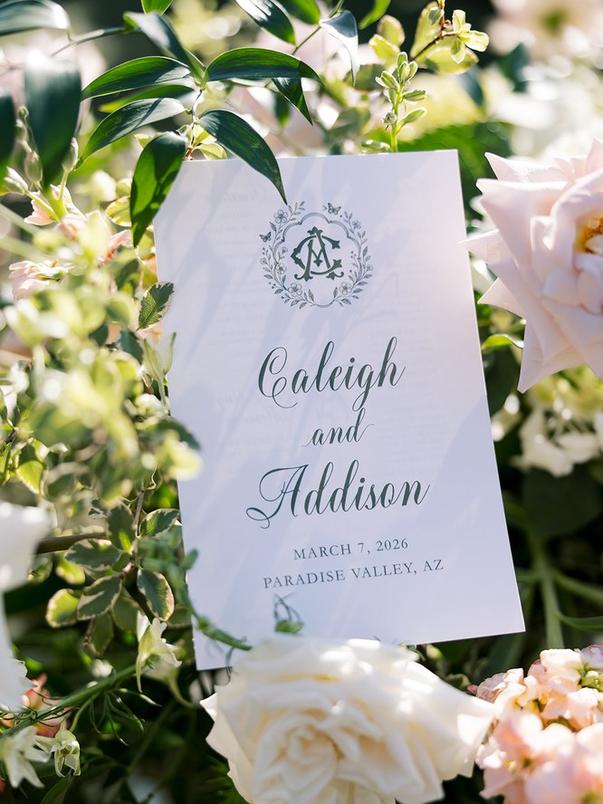 A wedding ceremony program for Caleigh and Addison, printed with a hand-drawn green monogram crest, nested in blush roses and greenery.